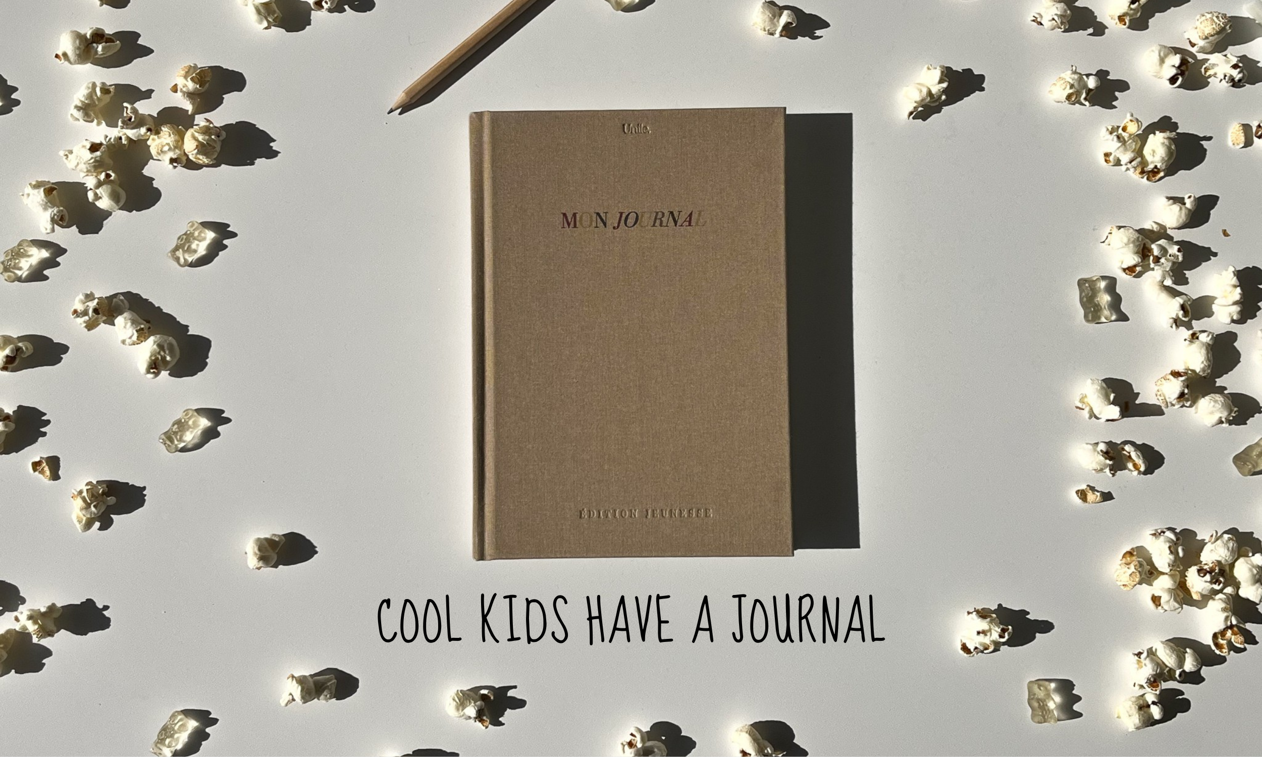 Le journal édition jeunesse Unile, entouré de bonbons et de pop-corns créant une ambiance aesthetic et graphique, suivi de la phrase engageante : cool kids have a journal.
