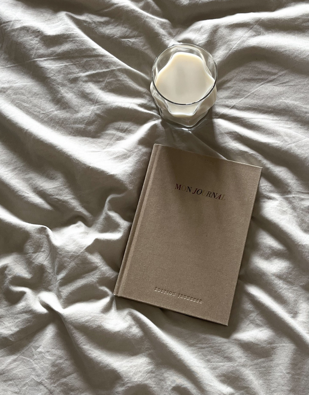 Journal édition jeunesse de face sur un lit, avec un verre de lait créant une ambiance apaisante et positive dès le matin.