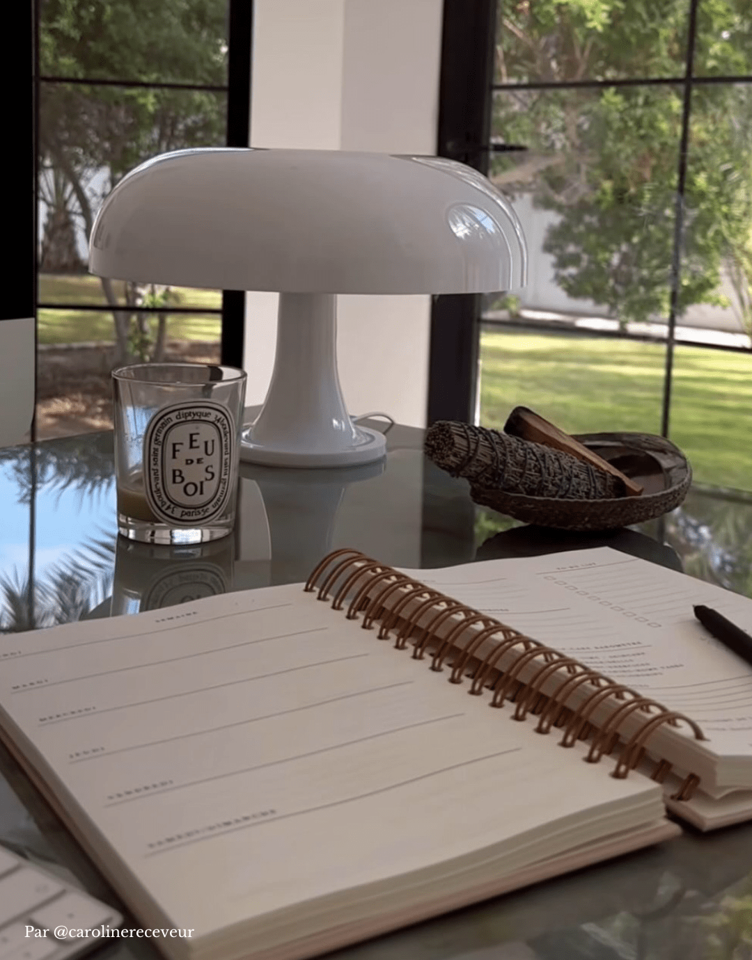 Planner Caroline Receveur Self-care planner spirales dorées ouvert sur la page du semainier et posé sur un bureau avec lampe Nessino, bougie feu de bois et palo santo en fond chez Caroline Receveur.