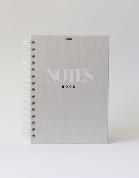 Notebook Unile.selfcare Notebook couverture en textile avec lettres gravées et spirales de face sur un fond uni.