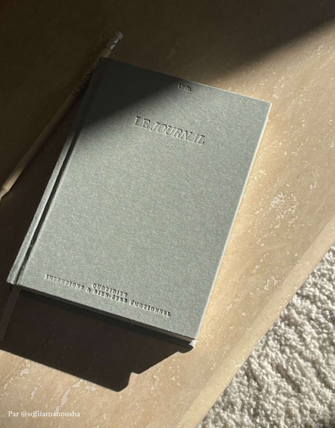 Journal - Unile Selfcare couverture en textile gris et lettres gravées posé sur une table en marbre avec jeux d'ombres.