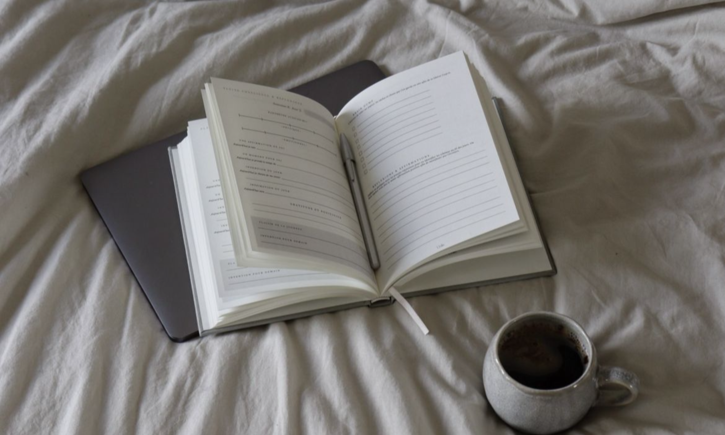 Carnet de journaling ouvert sur un lit à côté d'une tasse de café.