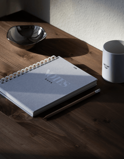 LE duo Notebook & Tasse - unile.selfcare carnet de notes à spirales et tasse blanche avec lettrage noir Self-care Club posés sur une table en bois