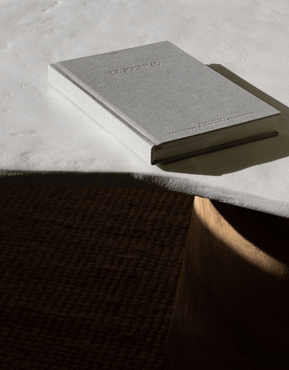 LE journal - unile.selfcare carnet de journaling gris en lettres gravées posé sur le coin d'une table avec jeu d'ombres et de lumière