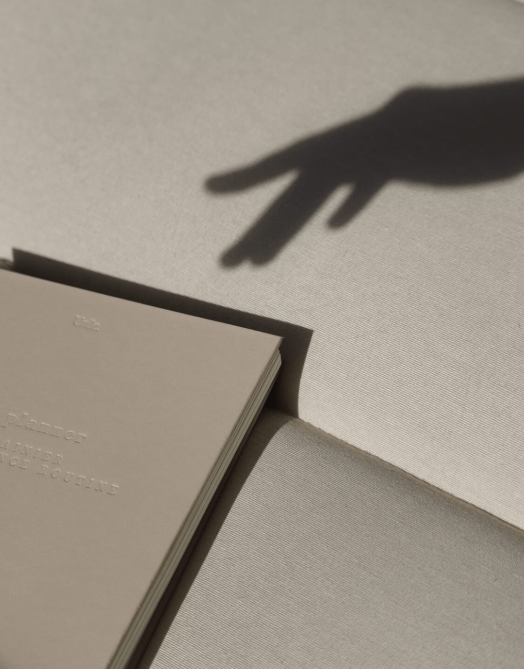 LE planner -version embossed - unile.selfcare planner beige avec lettres gravées avec ombre de main féminine en haut à droite