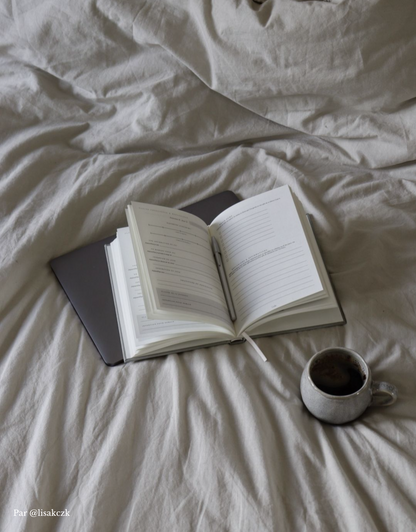 Journaling guidé en français, journal Unile Self care ouvert sur un lit à côté d'une tasse de café.