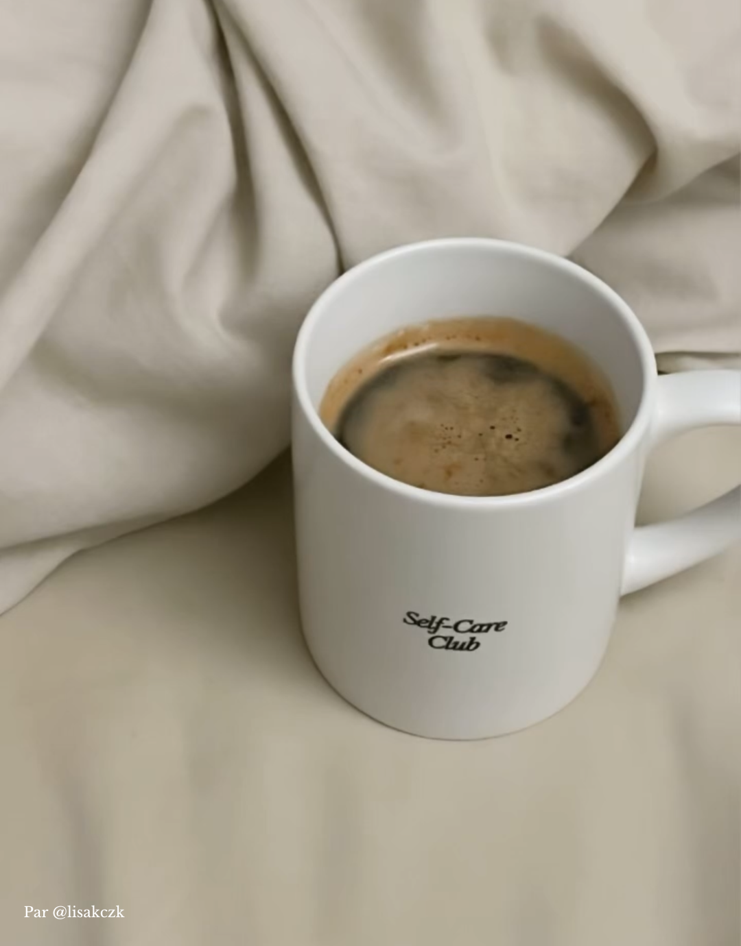 Tasse à café blanche en céramique Self-care Club posée sur des draps.